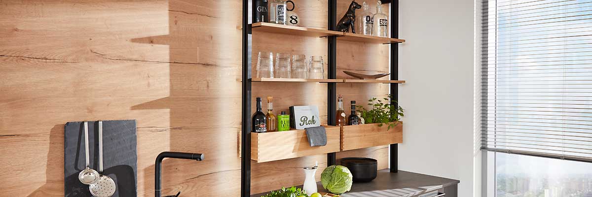 Moderne Küchenansicht mit Holzregalen an einer Wand, Geschirr, Gläser, Deko und Küchenutensilien, viel natürliches Licht durch große Fenster.